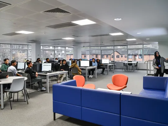 Computer classroom filled with students being taught by a female lecturer.